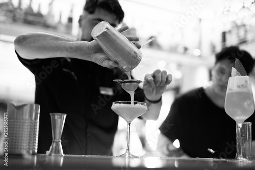 Photography Professional bartender straining a cocktail from a shaker into a coupe glass