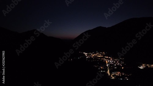 Bright lights of a serene village twinkling against the dark mountains under a tranquil evening sky