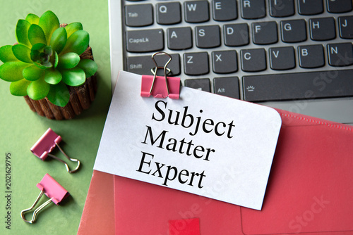 A red folder is lying on the table next to the laptop with the words SUBJECT MATTER EXPERT