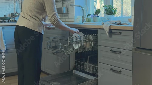 Woman removes clean dishes from dishwasher including plates and cups. Daily kitchen routine and household care.