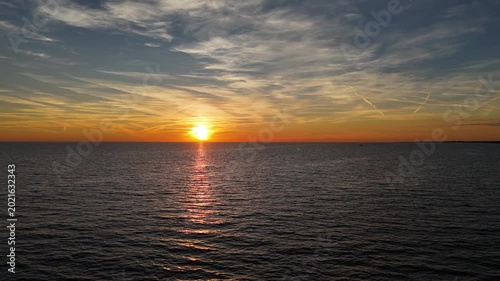 Golden sun descending over calm water as vibrant colors paint the evening sky near the shoreline
