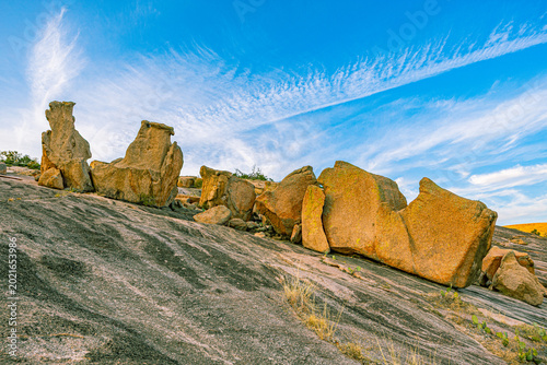 Fotografie A striking row of warm golden-orange granite boulders sits atop the striated bar