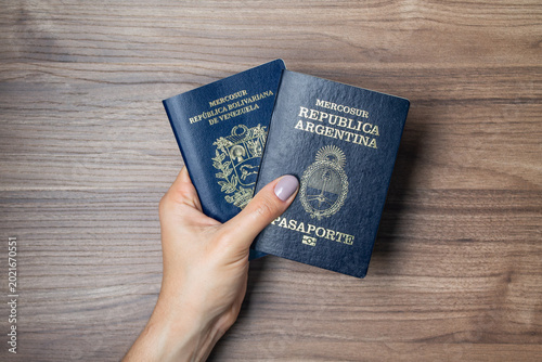 Konstfotografi Female hand holding Argentine and Venezuelan passports on a wooden background