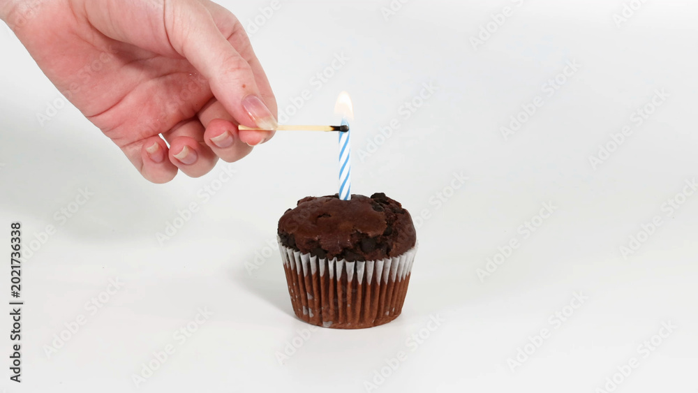Fototapeta premium Hand Lighting a Blue Striped Candle on a Chocolate Cupcake