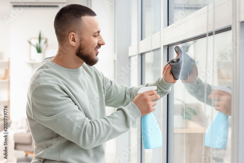 Young man cleaning large window at home