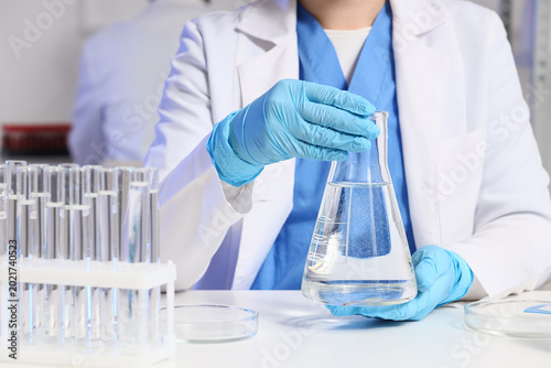Female scientist with test tubes and flask of water sample at table in labora...