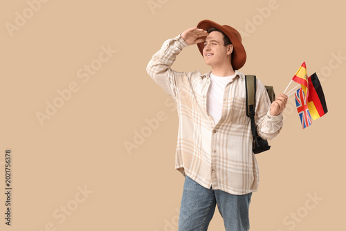 Young happy man with different flags and backpack on beige background