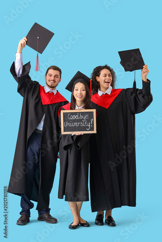 Graduate students holding chalkboard with text GOODBYE UNIVERSITY on blue bac...