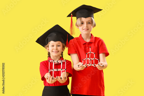 Little children in graduation hats with molecular models on yellow background...