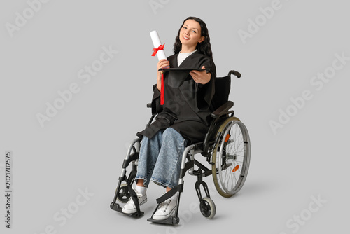 Beautiful female graduate student in wheelchair with graduation cap and diplo...