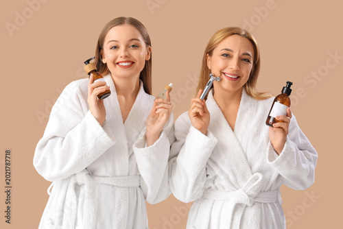 Valokuva Young woman and her mother in bathrobes with skincare products on beige backgrou