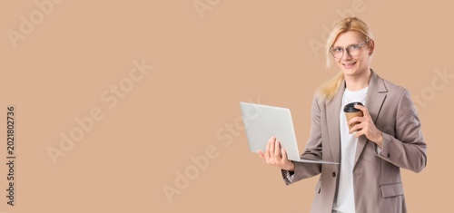 Young blond businessman with laptop and coffee on beige background with space...