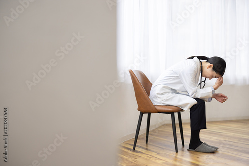 Fotografi Asian Female Doctor in White Coat Sitting with Head Down, Exhausted