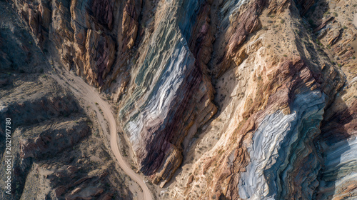 Aerial view of colorful stratified rock formations in a desert landscape with a winding road.
