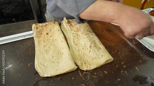 A cook places a meat kebab in an Arabic flatbread