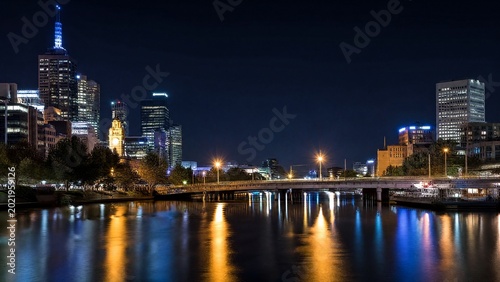 A nighttime cityscape glows with lights reflecting on the river, captured in a long exposure effect.