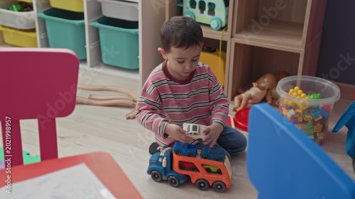 Boy playing with toy truck, hand on truck and smiling in a playroom inside building; joy imagination.