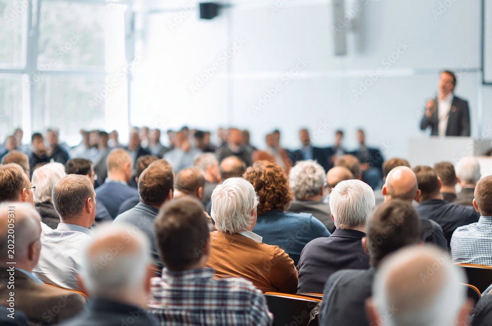 Obraz premium Diverse audience attends a business seminar with speaker presenting at the front of the room