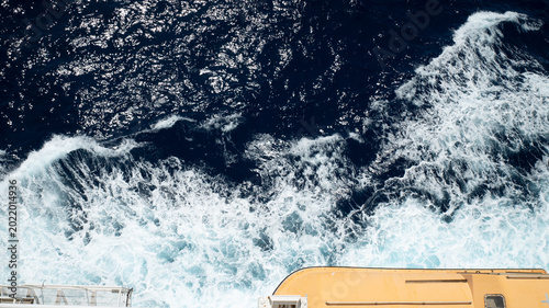 Tableau sur toile Dramatic aerial view of deep blue ocean waves and white sea foam with a partial yellow lifeboat in the foreground