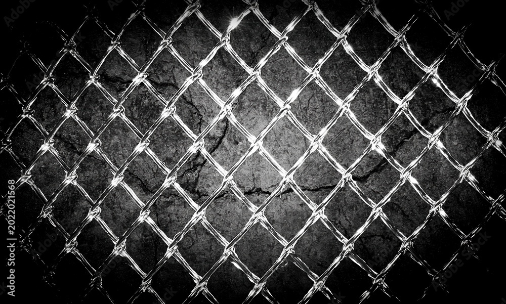 Fototapeta premium Close-up of a distressed, textured concrete wall behind a shining chain-link fence