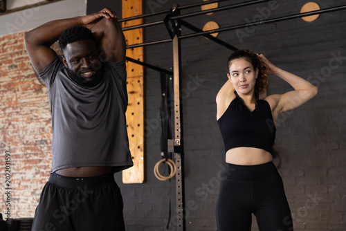 Cuadro en lienzo Diverse friends stretching in workout gear under pull-up rig in warehouse gym wi