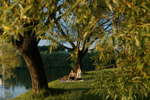 Two people enjoy a picnic by a peaceful pond surrounded by trees