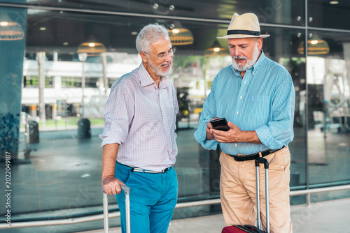 Fotografie Two senior men checking travel plans while looking at a smartphone at the airpor