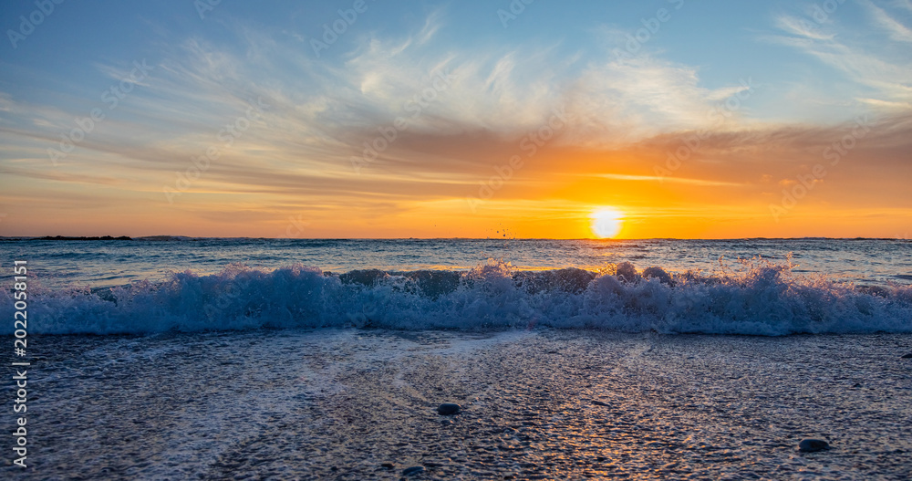 Obraz premium Dramatic Golden sunset over tranquil beach, waves lashing the pebble coastline