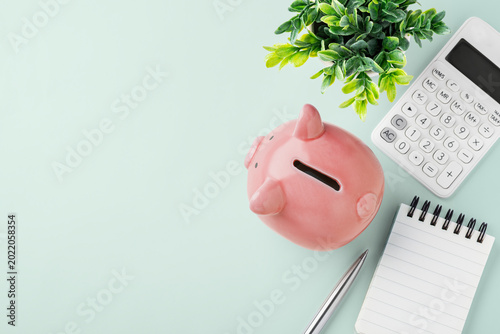 Pink piggy bank with calculator and spiral notebook on pastel green background, flatlay, finance planning, personal savings, and budgeting