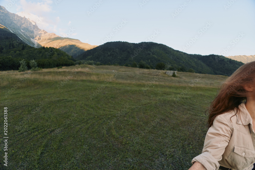 Fototapeta premium Woman lifestyle in an open field with distant mountains, natural landscape, casual beige jacket, feeling of freedom and outdoor exploration under a sunny sky