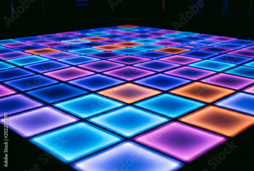 Grid of colorful glowing square lights on dance floor in dark night location.