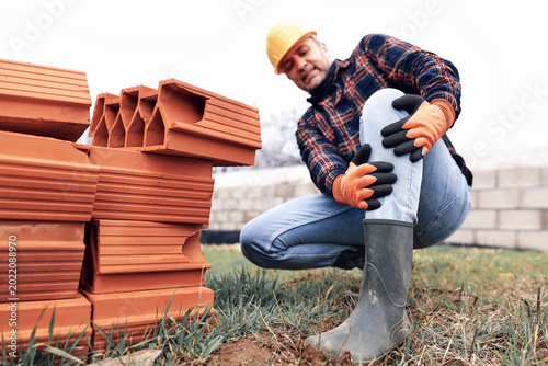 Photos Construction worker having a accident and injured knee and leg on a construction site outdoors