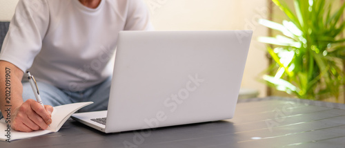Foto Person working remotely on laptop and writing notes in a notebook on an outdoor