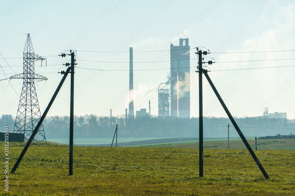 Fototapeta premium A large petrochemical enterprise on the background of a wheat field. Next to the agricultural field there's a factory for the production of chemical fertilizers. smoke escapes from factory chimneys