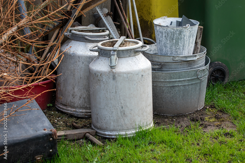 Obraz premium Old Metal Containers and Scrap Materials Stored Outdoors Near Garden Area