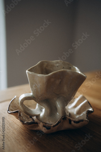 Beige handmade ceramic coffee set with a crumpled cup and a flower-shaped saucer with wavy edges.