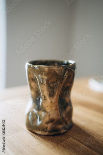Small handmade ceramic vase with a crumpled shape, featuring a distressed green and beige reactive glaze with a weathered.