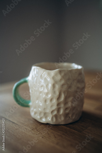 White handmade ceramic mug with a crumpled shape and a dimpled texture of indented dots across the surface.