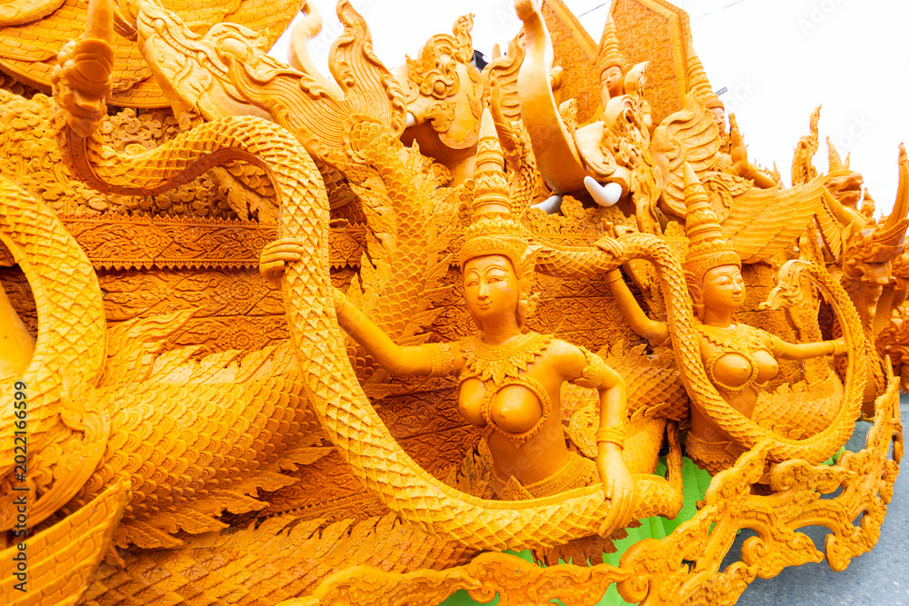 Obraz premium Stunning yellow wax sculpture featuring beautiful mythical female figures holding a Naga tail during a candle parade.