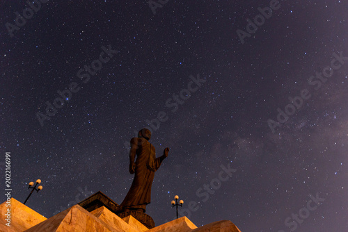 Принти на полотні Majestic standing Buddha statue silhouetted against a breathtaking night sky filled with countless glowing stars