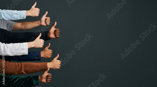 Diverse group of people giving thumbs up gesture against a dark background with copy space for success and approval concept.