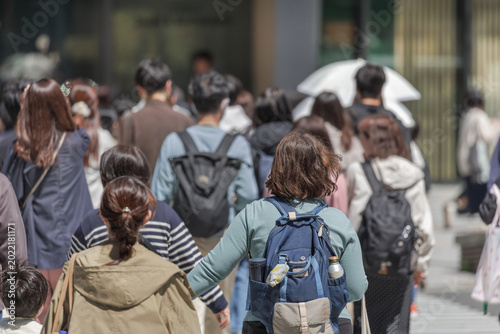 Quadro su tela Diverse group of people move along sunny city street as a collective flow of bodies, unconsciously aligning their pace with those around them