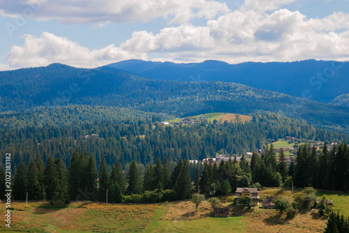 Picturesque mountain landscape. Ukrainian Carpathians. A cozy village lies in the valley below, surrounded by rolling green hills and misty mountain peaks. Bright traditional houses and untouched