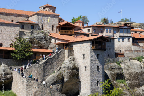 Bild auf Leinwand panoramic view of the great meteoron monastery in greece, featuring ancient stone architecture, terracotta roofs, and pilgrims climbing stairs carved into rocks