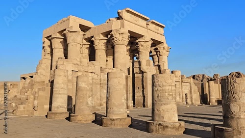 Kom Ombo temple ruins with double columns and composite capitals against clear blue sky in Egypt, ancient Ptolemaic architecture dedicated to Sobek and Horus with damaged walls.