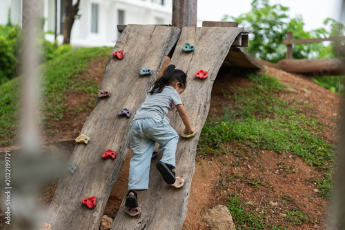 preschool child girl practicing climbing on wooden bouldering wall at outdoor playground