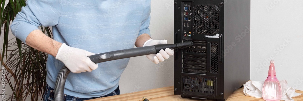 Φωτογραφία A 53-year-old man cleans dust from a computer system unit with a vacuum cleaner in a tidy room