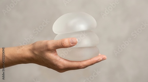 A hand holding silicone breast implants for plastic surgery consultation illustration