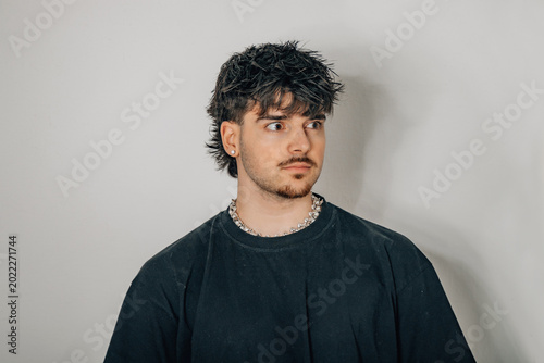 Canvastavla oung man with a dark textured mullet and chain necklace, glancing sideways against a neutral gray studio background