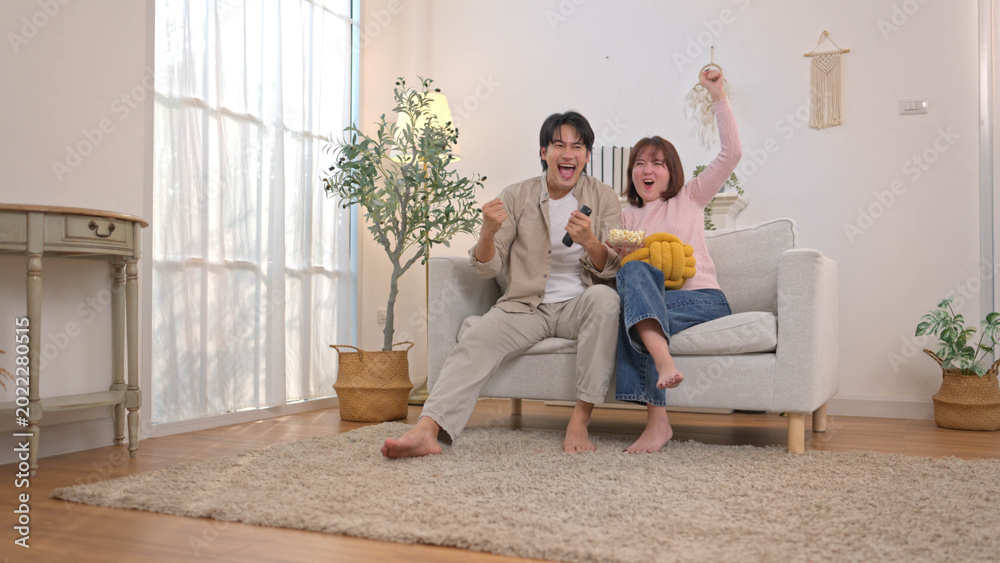 Obraz premium Excited young couple cheering on sofa while watching television